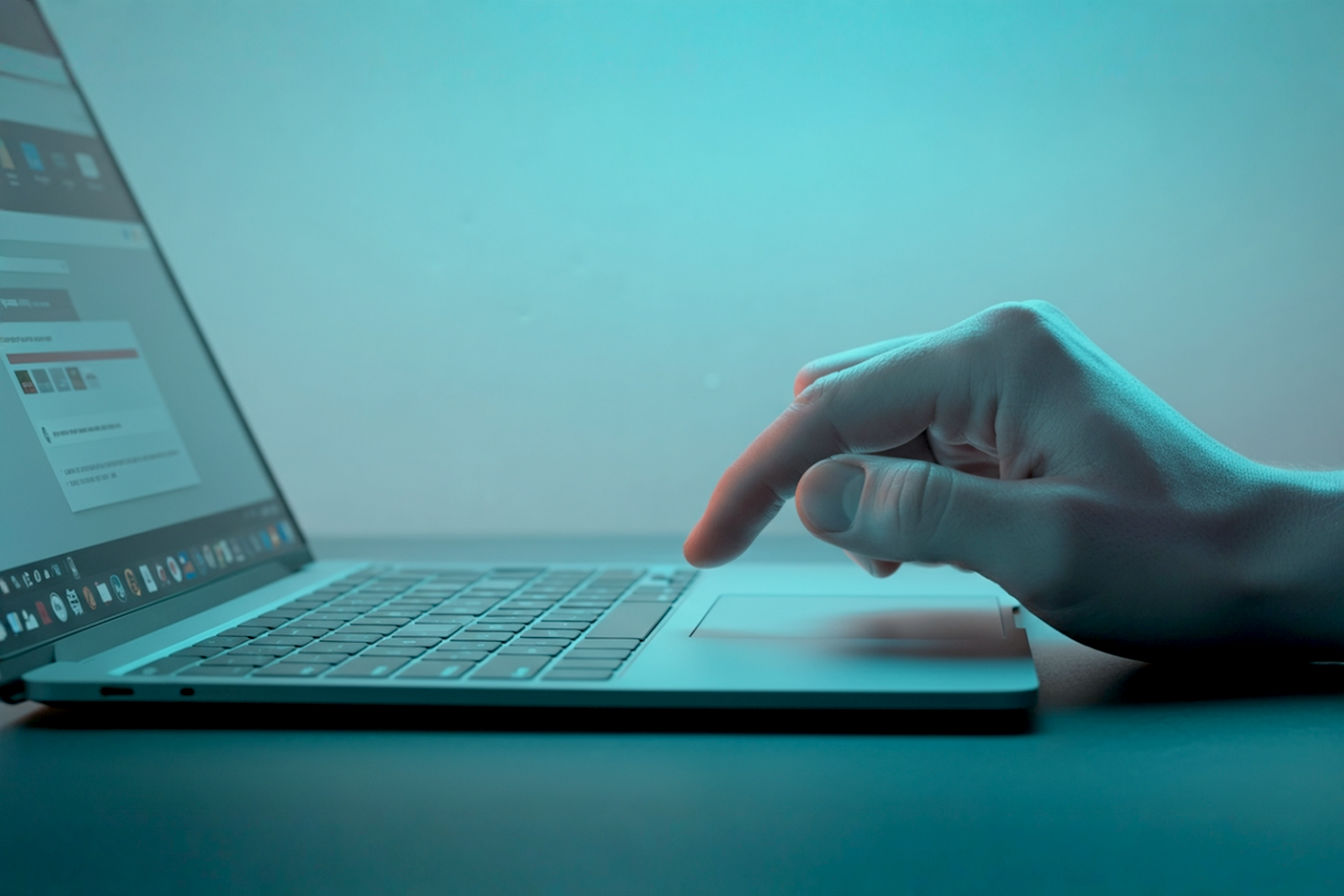 Professional, brightly lit, slightly desaturated, photorealistic image of a hand confidently using a modern laptop trackpad. The laptop screen, slightly out of focus in the background, displays a backup software interface. Focus on the hand and trackpad, conveying control and efficiency. Clean, minimalist background.